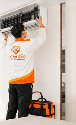 KindGo technician in orange and white uniform servicing a wall-mounted air conditioner